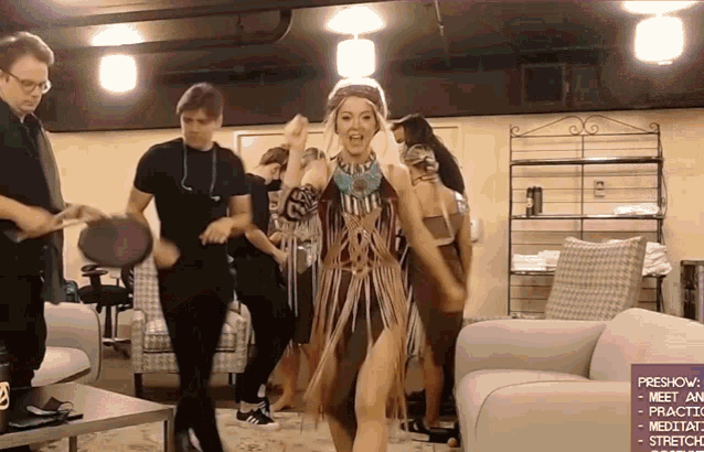 a woman in a native american outfit is dancing in a room with other people