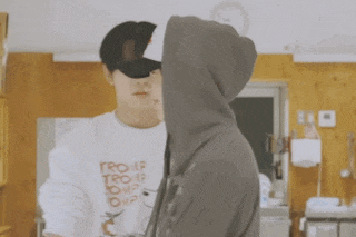 a man wearing a hat that says aloha is hugging another man in a hoodie