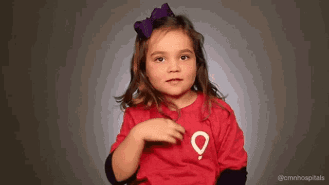 a little girl with a purple bow on her head is wearing a red shirt with a map on it .