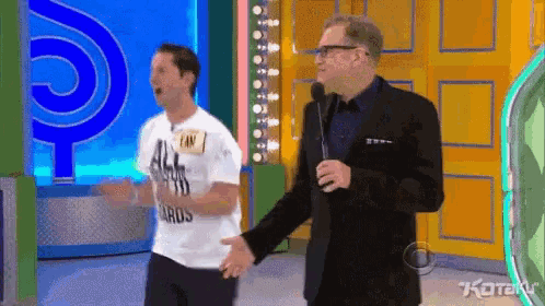 a man wearing a white shirt that says all i want is standing next to a man in a suit holding a microphone