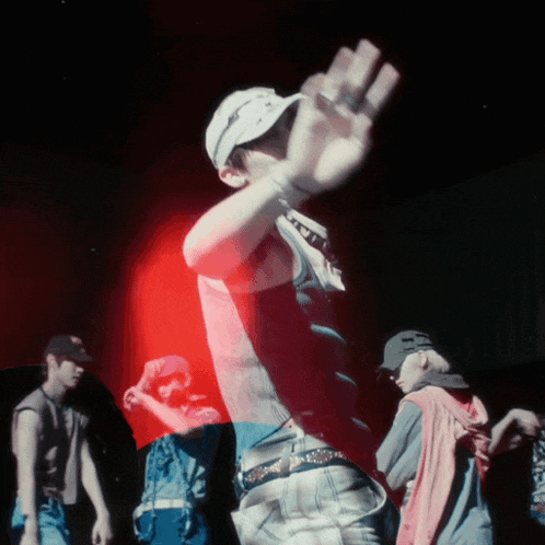 a man wearing a hat with the letter t on it stands in a dark room