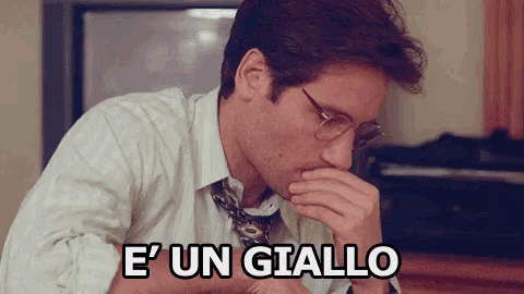 a man wearing glasses and a tie is covering his mouth with his hand and says e ' un giallo .