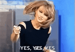 a woman in a black top is holding a cell phone in her hand and saying yes .