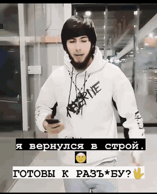 a man wearing a white hoodie with the word keferine on it is looking at his phone