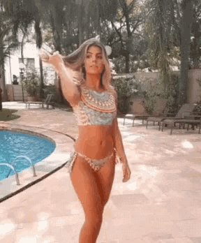 a woman in a bikini stands in front of a swimming pool