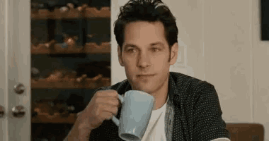 a man is sitting at a table drinking from a blue mug .