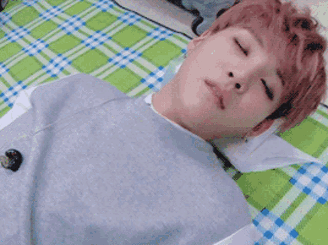 a young man with pink hair is laying on a green and white checkered blanket with his eyes closed