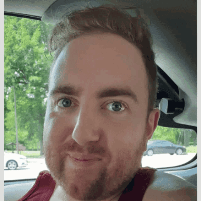 a man with a beard and a red tank top looks at the camera