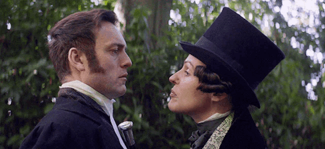 a man in a top hat and a woman in a tuxedo are looking at each other