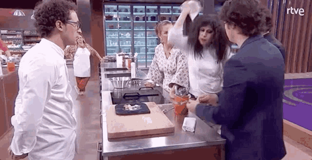 a group of people are standing around a cutting board in a kitchen and talking to each other .