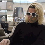 a woman wearing sunglasses and a black turtleneck is sitting in a living room .