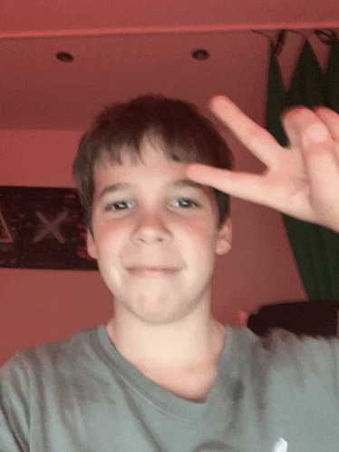 a young boy giving a peace sign in front of a x on a wall