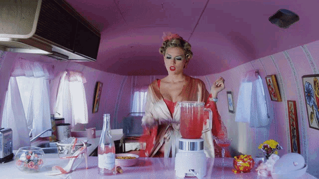 a woman is making a drink with a blender in a pink room