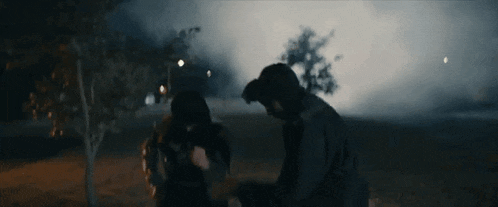 a man and a woman are standing next to each other in a dark field at night .