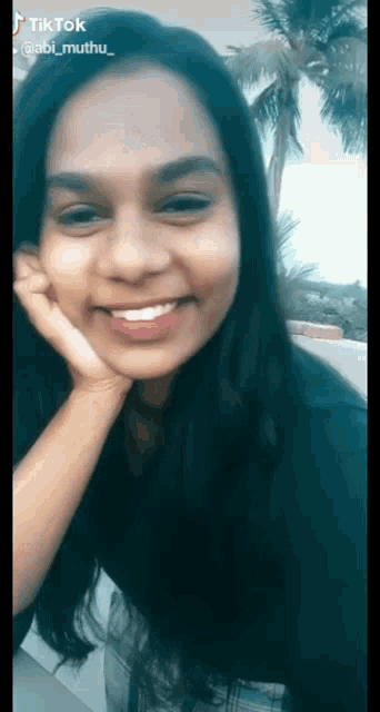 a woman with long black hair is smiling with her hand on her face and the name abi muthu on the bottom