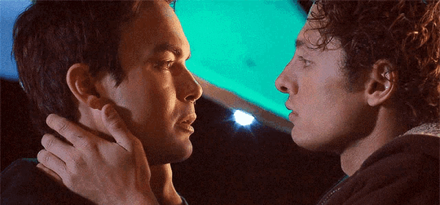 two men are touching each other 's faces in front of a green light