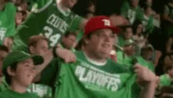 a man wearing a red hat and a green shirt that says playoffs is standing in a crowd of people .