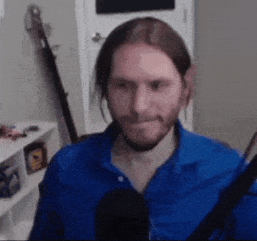a man with long hair and a beard is sitting in front of a microphone and making a funny face .