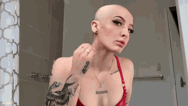 a woman with a shaved head and a lot of tattoos is standing in a bathroom .