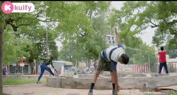 a man is doing a handstand in a park while another man stands behind him .