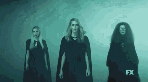 three women in black dresses and capes are standing next to each other in a foggy room .