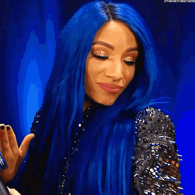 a woman with blue hair is wearing a black jacket with spikes on it