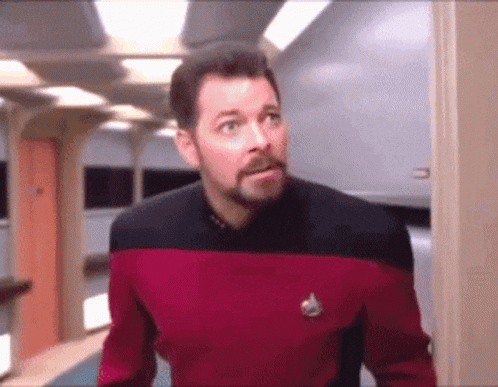 a man with a beard is wearing a red and black uniform and has a star trek logo on his chest .