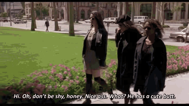 three women are walking down a sidewalk and one of them is talking about a man 's butt