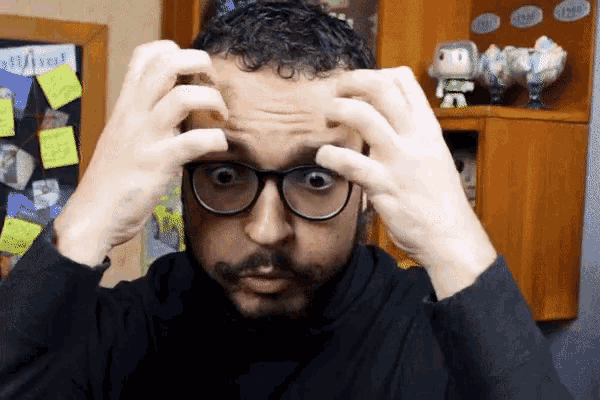 a man with glasses and a beard is scratching his head with his hands
