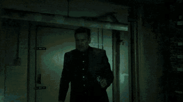 a man in a black jacket stands in a dark room with a green light shining on him