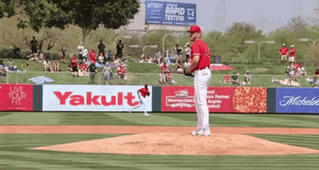 a baseball pitcher winds up to throw a ball in front of a yakult sign