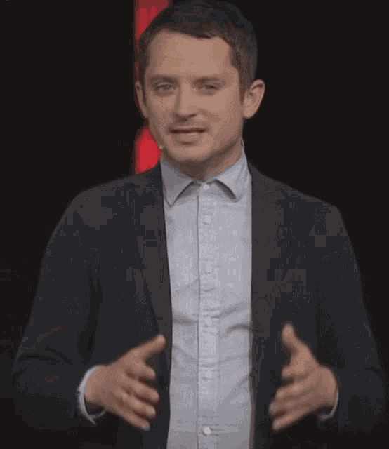 a man wearing a suit and a grey shirt is giving a presentation