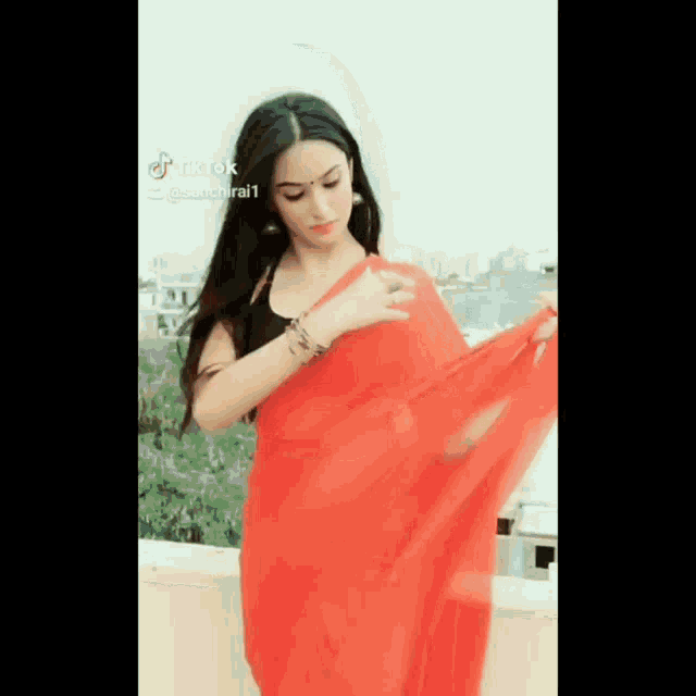 a woman in a red saree is standing on a rooftop .