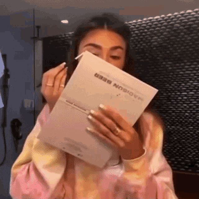 a woman in a tie dye sweatshirt is applying makeup while holding a box of makeup .