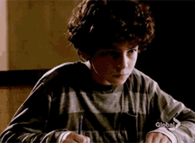 a young boy is writing on a piece of paper with a globe tv logo on his left hand