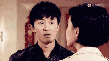 a man and a woman are looking at each other in a room . the man is wearing a leather jacket .