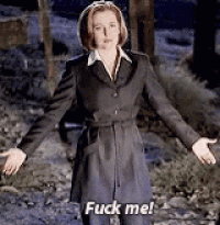 a woman in a trench coat is standing in the woods with her arms outstretched and saying `` fuck me '' .