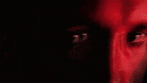 a close up of a person 's eyes in the dark with a red background .