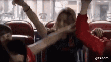 a group of people are sitting on a bus with their arms up in the air .