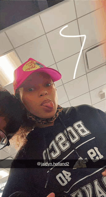 a woman wearing a pink hat and a black shirt with the word holland on it sticks her tongue out
