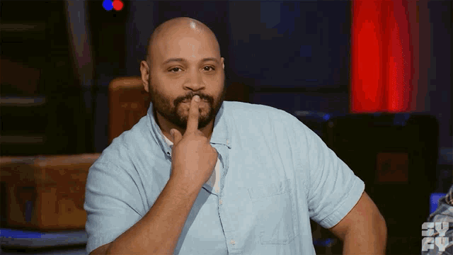 a bald man with a beard holds his finger to his chin