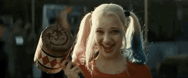 harley quinn from suicide squad is holding a wooden mallet and smiling .