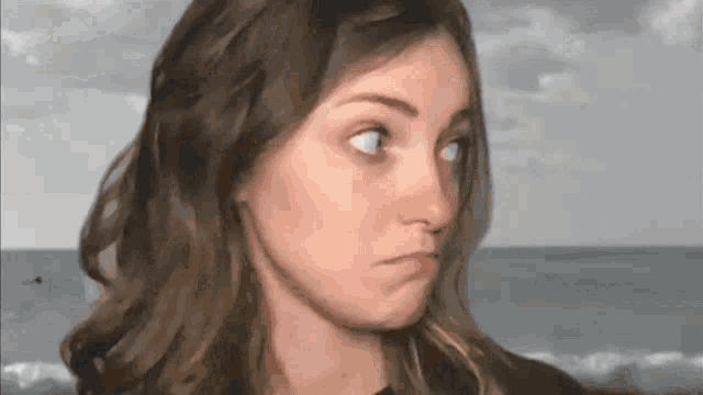a close up of a woman making a funny face with the ocean in the background