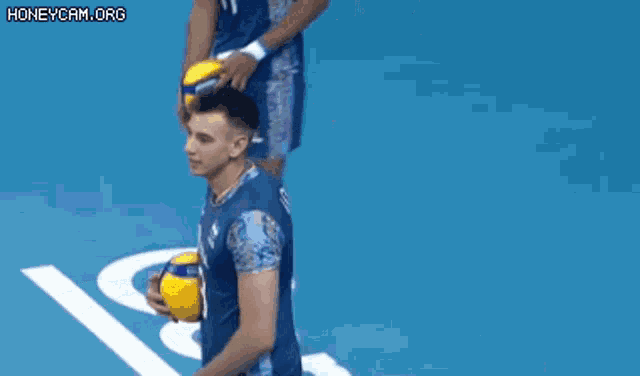 a man in a blue shirt is holding a volleyball on a blue surface .