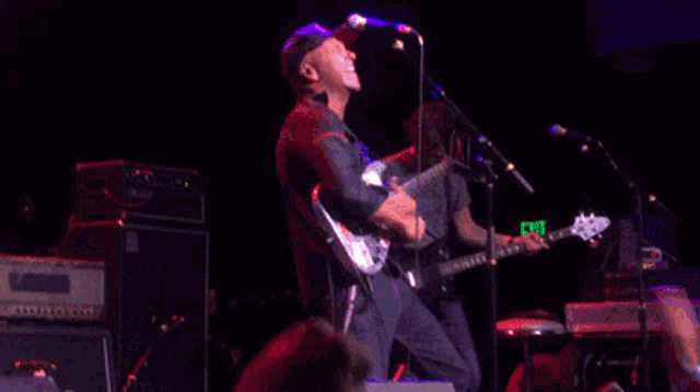 a man playing a guitar on a stage with a green exit sign in the background
