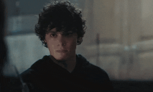 a young man with curly hair looks at the camera with a serious look on his face