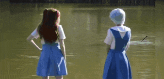two women in blue dresses are standing next to a body of water holding a cat .