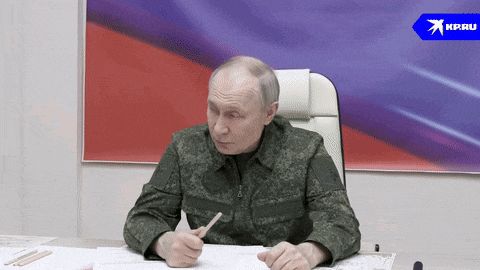 a man in a military uniform sits at a desk in front of a flag and a sign that says kp.ru