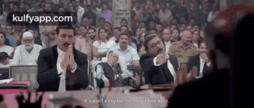 a group of men are sitting in front of a large crowd in a courtroom .