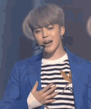 a young man wearing a blue jacket and a striped shirt is holding a microphone and smiling .